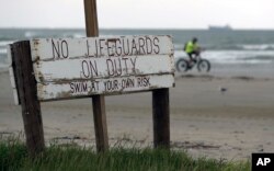 A cyclist passes a weathered sign along the beach in Port Aransas, Texas, Sept. 29, 2017.