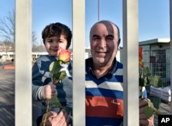 Migrants hold flowers behind the fence of a refugee home in Cologne, Germany, Jan. 22, 2016.