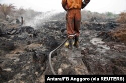 Seorang petugas pemadam kebakaran dari Badan Penanggulangan Bencana Daerah mencoba memadamkan kebakaran lahan gambut di perkebunan kelapa sawit di Pelalawan, Provinsi Riau, 26 September 2015. (Foto: Antara/FB Anggoro via REUTERS)