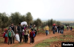 FILE - Internally displaced people walk with their belongings in the town of Inab, eastern Afrin, Syria, March 14, 2018.
