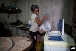 Carmen Rivero fills her washing machine with a bucket of water at her home during water shortages in the Petare shantytown of Caracas, Venezuela, June 7, 2018.