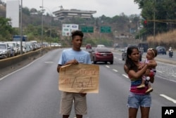 FILE - A demonstrator from Las Minitas shantytown holds up a poster that reads in Spanish "Four weeks without water" after water service was suspended, on the Prados del Este highway in the Santa Fe neighborhood of Caracas, Venezuela, April 27, 2018.