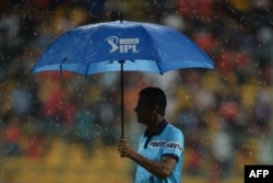 FILE - An umpire carries an umbrella as he walks onto the playing area for a ground inspection as rain delays the start of the 2019 Indian Premier League (IPL). (Photo by Manjunath KIRAN / AFP)