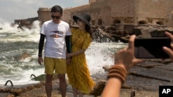 In this Aug. 8, 2019, photo, a couple poses for a portrait on cement blocks placed as reinforcement against rising water levels near the citadel in Alexandria, Egypt. (AP Photo/Maya Alleruzzo)