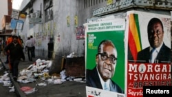 Election campaign posters are pictured near Zimbabweans walking on a street blocked by uncollected garbage in Harare July 17, 2013.