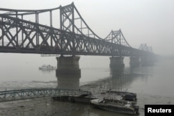 FILE - Trucks move across the bridge linking North Korea with the Chinese border city of Dandong, March 3, 2016. Experts says China is facing a delicate balancing act with sanctions as Pyongyang might use its nuclear and missile capabilities to threaten Beijing.