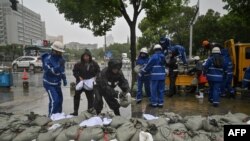 Sekelompok warga menempatkan karung pasir di sebelah sungai Yuyao di Ningbo, provinsi Zhejiang China timur, saat Topan In-Fa menerjang pantai timur China, 25 Juli 2021. (Foto: Hector RETAMAL / AFP)
