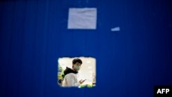 A store worker wearing a face mask as a preventive measure against the COVID-19 coronavirus waits for costumers behind a barrier in Wuhan, in China's central Hubei province, April 1, 2020. 