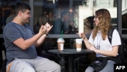 Sign language interpretation major,student Nikolas Carapellatti (L) signs with deaf Gallaudet University student Rebecca Witzofsky outside the first US Starbucks café staffed by employees who are partially or fully deaf and capable of communicating in American Sign Language. AFP
