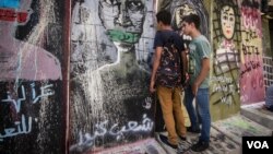 Young Lebanese peer through a gap in the wall, which was erected Monday in Beirut in the wake of clashes with protesters over the weekend. (Credit: John Owens/VOA)