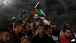 Protesters chant slogans while waving their national flags as others burn tires near the fence of the Gaza Strip border with Israel during a protest east of Gaza City, Oct. 26, 2018. 