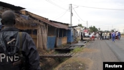 A policeman watches from a distance as residents gather near the bodies of unidentified men killed during gunfire, in the Nyakabiga neighborhood of Burundi's capital Bujumbura, Dec. 12, 2015.
