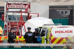 Police officers are on the scene after a truck, in rear, was found to contain 39 dead bodies, found to be Vietnamese nationals, near London, England, Oct. 23, 2019.