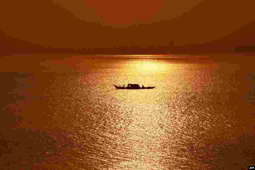 A fishing boat travels along the Mekong River as the sun rises over Phnom Penh, Cambodia.