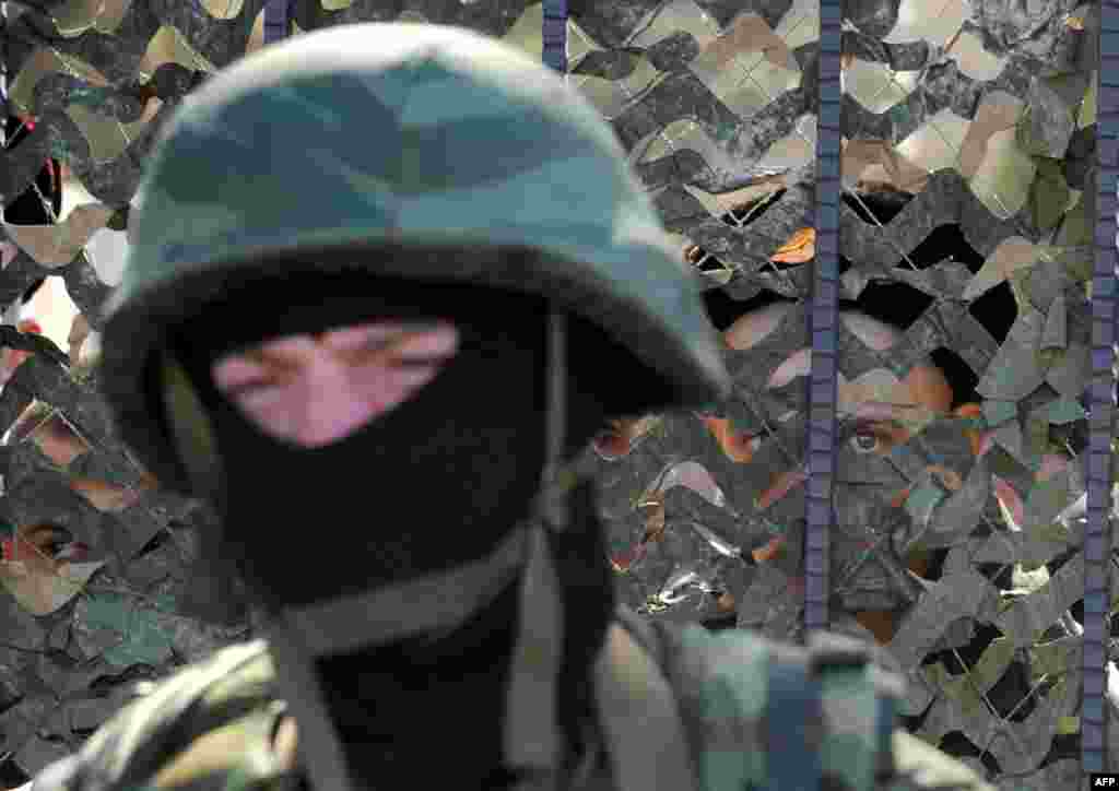 A Ukrainian soldier stands behind a fence while unidentified armed men block the headquarters of the Ukrainian Navy in Sevastopol.