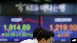 A currency trader watches the computer monitors near the screens showing the Korea Composite Stock Price Index (KOSPI), left, and the foreign exchange rate between U.S. dollar and South Korean won at the foreign exchange dealing room in Seoul, South Korea.