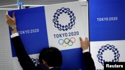 Seorang staf menurunkan spanduk bertuliskan Tokyo 2020 Olympics setelah konferensi pers. (Foto:dok)