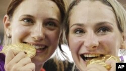 Atlet Jerman Kristina Vogel (kanan) dan teman satu tim Miriam Welte menggigit medali emas yang dimenangkan dalam nomor sepeda trek cepat putri di London. (Foto: AP)