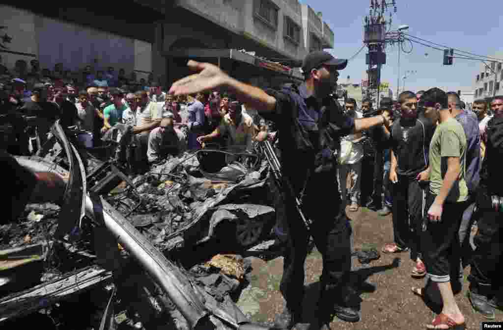 A police officer gestures as Palestinians inspect the remains of a car which police said was targeted in an Israeli air strike in Gaza City, July 8, 2014.