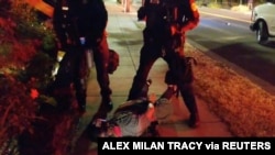 Journalist Justin Yau lies handcuffed on the ground with police officers standing beside him, after they dispersed protesters during a demonstration against racial injustices in Portland, July 1, 2020 in this still image obtained from social media video.