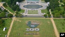 People on the National Mall in Washington, looking toward the World War II Memorial, Aug. 25, 2016, recreate a giant, living version of the National Park Service emblem, using brown, green and white umbrellas. 
