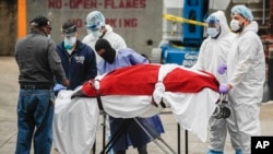 A body wrapped in plastic that was unloaded from a refrigerated truck is handled by medical workers wearing personal protective equipment due to COVID-19 concerns, Tuesday, March 31, 2020, at Brooklyn Hospital Center in Brooklyn borough of New York. (AP Photo/John Minchillo)