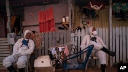 Welington Goncalves, right, sits next to his colleague as they wait to refill their tanks during a disinfection to help contain the spread of the new coronavirus in an area occupied by squatters in Rio de Janeiro, Brazil, June 26, 2020.