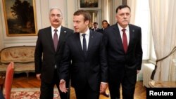 Presiden Perancis Emmanuel Macron (tengah) berjalan bersama PM LIbya Fayez al-Sarraj (kanan) dan Jenderal Khalifa Haftar sebelum pertemuan di Paris, Selasa (25/7). 