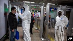 A worker wearing a hazardous materials suit takes the temperature of a passenger at the entrance to a subway station in Beijing, Jan. 26, 2020. 