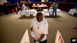 Darren Atkinson wears a mask as he wipes down a voting booth at a voting center during primary voting in Washington, June 2, 2020.