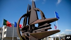 FILE - The NATO symbol and flags of member nations are seen outside of the alliance's headquarters in Brussels.