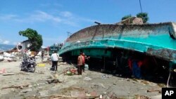 Warga menyaksikan kapal yang terdampar diterjang tsunami di Palu, Sulawesi Tengah, Minggu, 30 September 2018.