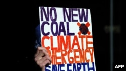 An environmental activist from Extinction Rebellion holds up a placard during a protest against the India-backed Adani coal mine project, outside the GHD engineering office building in Sydney, Aug. 13, 2019. - Scores of environment advocates occupied…
