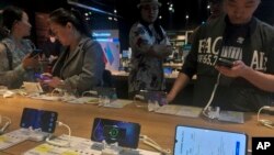 FILE - People try out Huawei smartphones on display at an electronics store in Beijing, May 20, 2019.