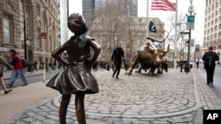 A statue titled "Fearless Girl" faces the Wall Street bull, March 8, 2017, in New York. A big investment firm, State Street Global Advisors, put the statue there to highlight International Women's Day. The work by artist Kristen Visbal. 