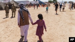 FILE - A man walks with a child through Fort Bliss' Doña Ana Village where Afghan refugees were being housed, in New Mexico, Sept. 10, 2021. 