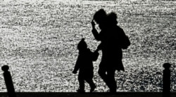 A mother and a child walk in the evening sun at a lake in Gelsenkirchen, Germany, March 22, 2020. To slow the spread of the coronavirus, Germany has considerably restricted public life and asked citizens to observe social distancing and stay home.
