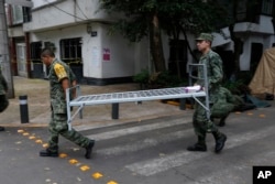 Soldiers carry a cot as they break camp from earthquake-torn Condesa neighborhood of Mexico City, Oct. 3, 2017.