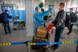 A worker in a protective suit takes the temperature of a traveler at Beijing Capital International Airport in Beijing, March 6, 2020.