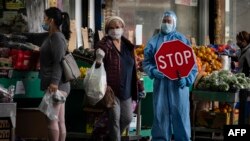 រូបឯកសារ៖ បុគ្គលិកម្នាក់ពាក់សម្លៀកបំពាក់ការពារខ្លួនពីមេរោគជួយសម្រួលដល់អតិថិជនមកទិញម្ហូបអាហារ នៅតំបន់រស់នៅមួយ នៅក្រុងញូវយ៉ក កាលពីថ្ងៃទី១៨ ខែឧសភា ឆ្នាំ២០២០។ 