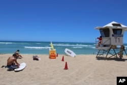 A surfer waxes his board on the sand at a beach known as White Plains in Ewa Beach, Hawaii, on May 12, 2023. (AP Photo/Jennifer Sinco Kelleher)