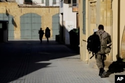 FILE - A Greek Cypriot soldier (R) walks towards a military guard post across the U.N. buffer zone that divides the Greek and Turkish Cypriots controlled areas, in the divided capital of Nicosia, Cyprus, Jan. 12, 2017.