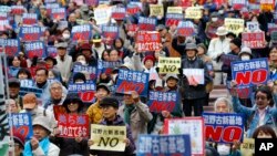 ក្រុមបាតុករ​ប្រឆាំង​នឹង​មូលដ្ឋាន​យោធា​អាមេរិក​ កាន់​បដាប្រកាស​ដែល​មាន​ពាក្យស្លោក​សរសេរថា​ «និយាយ​ថា​ទេ ចំពោះ​មូលដ្ឋាន​ទ័ព​ថ្មី​នៅ​តំបន់​ Henoko» ក្នុង​អំឡុង​ពេល​ធ្វើបាតុកម្ម​កាលពី​ថ្ងៃទី​២៩ ខែវិច្ឆិកា ឆ្នាំ២០១៥។