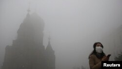 Seorang wanita mengenakan masker saat melewati gereja San Sophia di kota Harbin, China yang tertutup kabut tebal akibat asap polusi (21/10). 