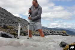 FILE - Scientist Oliver Grah measures the speed of a melt water stream from Sholes Glacier on one of the slopes on Mount Baker in Washington, Aug. 7, 2015. Glaciers on this and other mountains in the North Cascades are thinning and retreating.