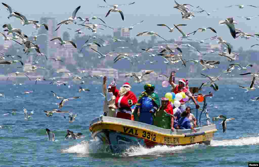 2017年12月24日，圣诞节前夕，智利瓦尔帕莱索海岸附近，一位穿着圣诞老人服装的男子在渔夫的船上挥手致意。