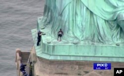 In this image made from video by WPIX, Therese Okoumou, center, leans against the robes of the Statue of Liberty on Liberty Island, as a police officer stands on a ledge nearby, talking her into descending, in New York, July 4, 2018.