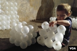 Naomi, 2, is enjoying picking up the cubes and tossing them around. (D. Block/VOA)