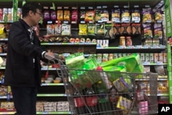FILE - A man pushes a shopping cart past a display of nuts imported from the United States and other countries at a supermarket in Beijing, April 2, 2018.