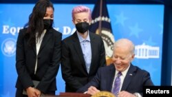 សមាជិក​ក្រុម​បាល់​ទាត់​ជាតិ​ស្ត្រី​របស់​ស.រ.អ អ្នកនាង Margaret Purce និង​អ្នកនាង Megan Rapinoe ឈរ​នៅក្បែរ​លោកប្រធានាធិបតី Joe Biden នៅពេល​ដែល​លោក​ចុះហត្ថលេខា​លើ​សេចក្តី​ប្រកាស​ទិវា​បៀវត្សរ៍​ស្មើគ្នា​នៅ​ឯ​សេតវិមាន​ក្នុង​រដ្ឋធានី​វ៉ាស៊ីនតោន នៅ​ថ្ងៃទី២៤ ខែមីនា ឆ្នាំ២០២១។